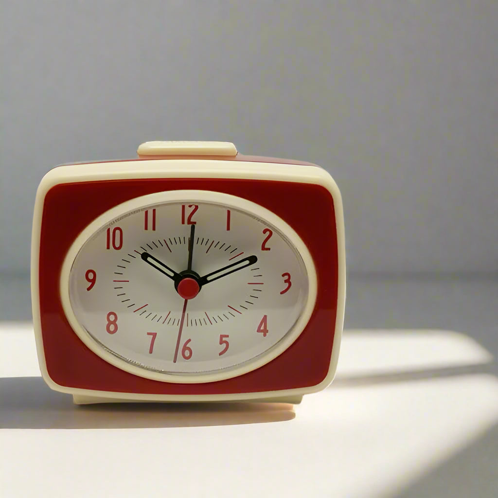 Red and beige vintage-style alarm clock on a white surface with a neutral background