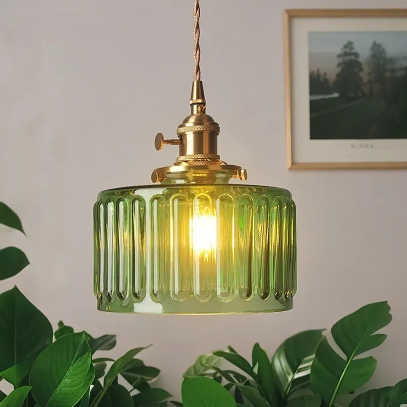 Green ribbed pendant light with gold fixture on a neutral wall with a plant and framed picture in the background.