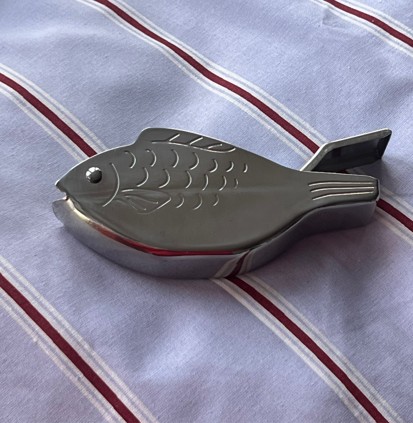 Metallic fish-shaped object on a striped fabric background