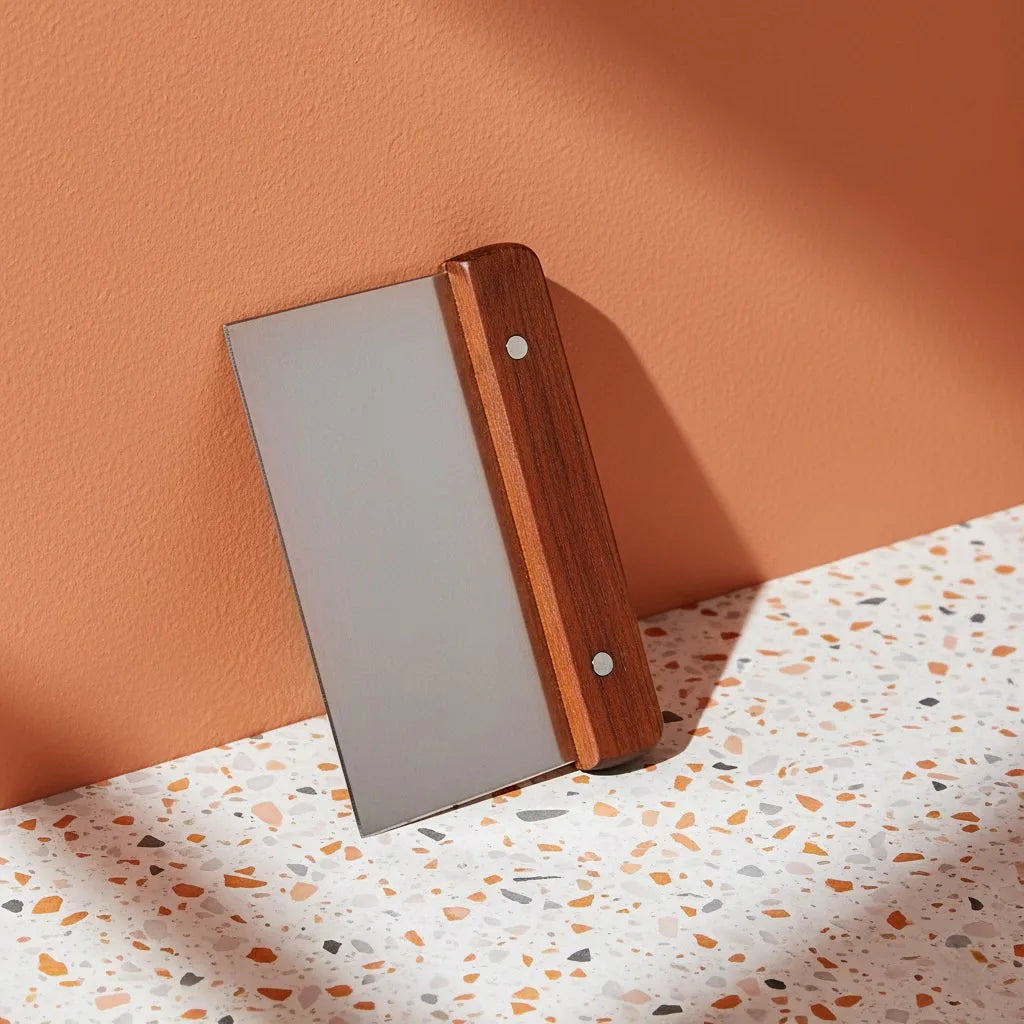 A dough scraper propped against a wall. Terrazzo surface with teracotta painted wall and warm light.