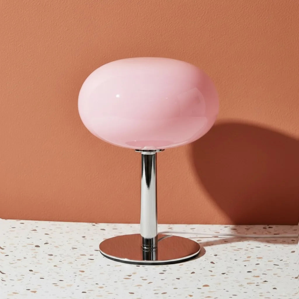 Pink table lamp with a metallic base on a terrazzo surface against a peach wall.