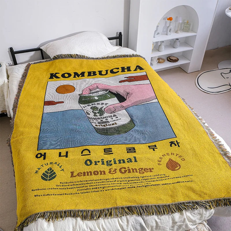 Yellow blanket with kombucha design draped over a bed in a room.