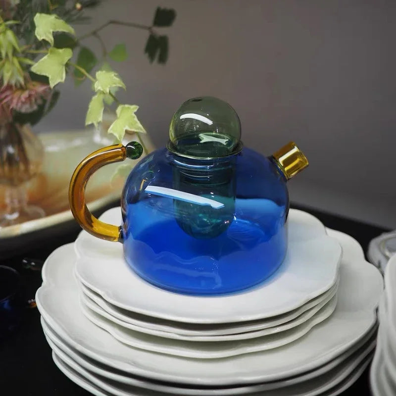 Blue glass teapot with a gold handle on a stack of white plates.