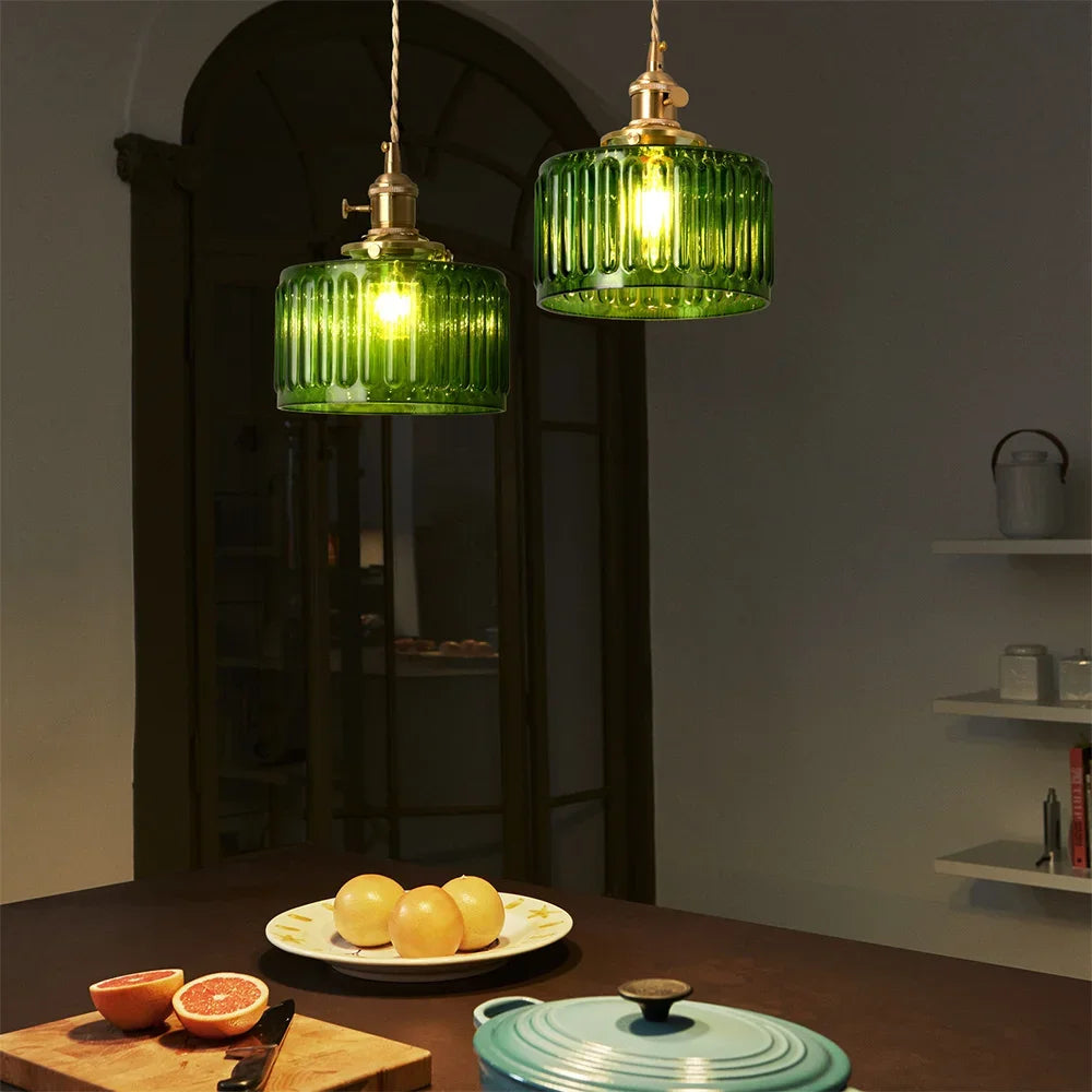 Two green pendant lights hanging above a table with fruits and a pot.