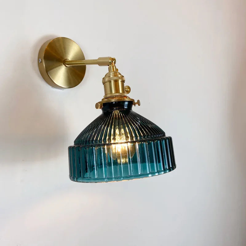 Wall-mounted light fixture with brass arm and blue glass shade on a white wall.