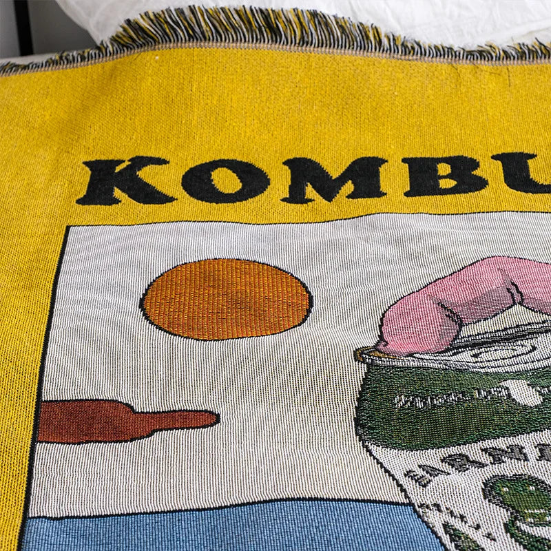 Textile with 'KOMBU' and images of a bun, hand, and can on a yellow background