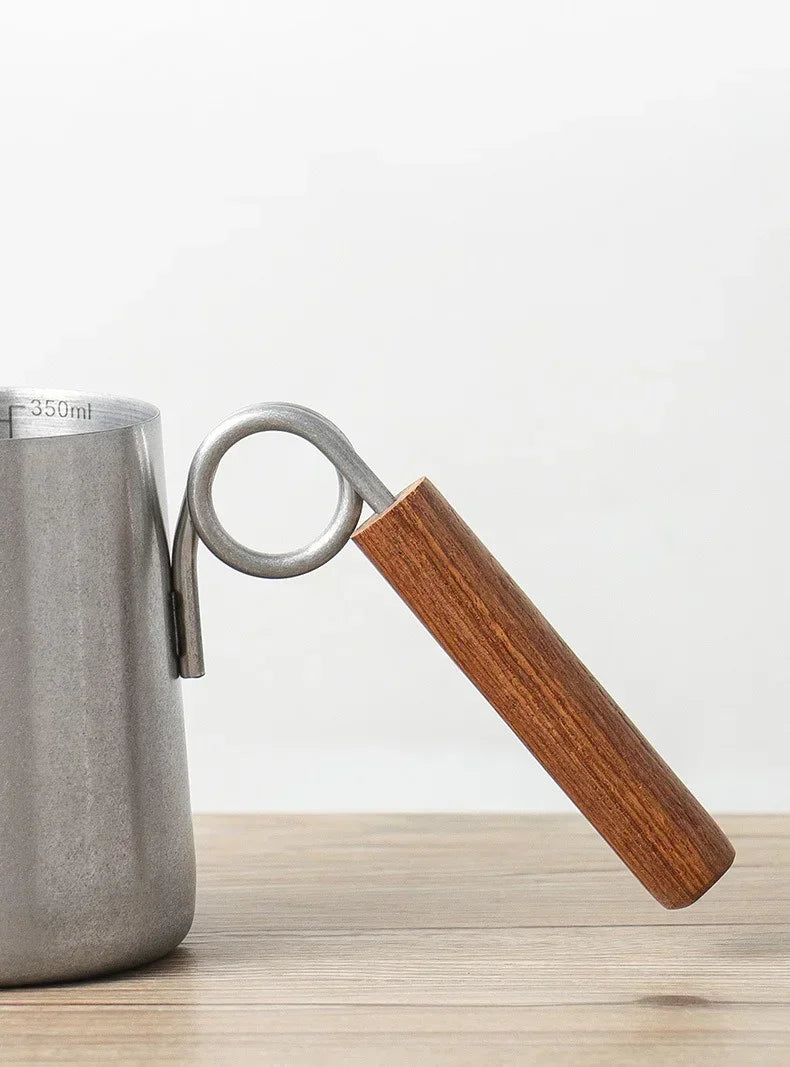 Metal pitcher with wooden handle on a light wooden surface