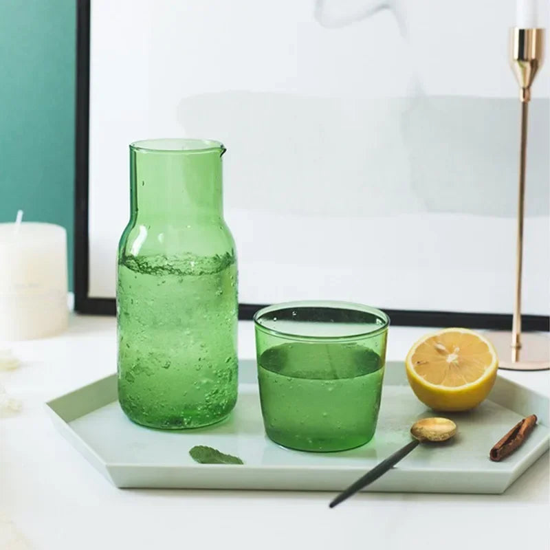 Green glass carafe and cup on a white tray with lemon and cinnamon.