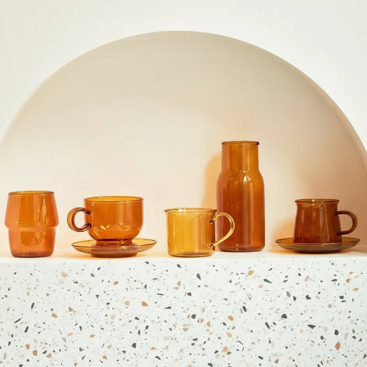 Set of orange ceramic cups and a carafe on a white surface with a neutral background
