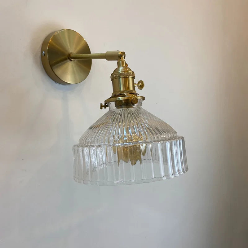 Brass wall-mounted light fixture with clear glass shade on a plain background