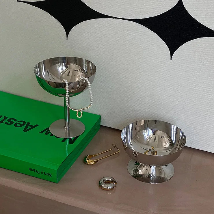 Two metallic bowls on a surface with a green book and decorative items.
