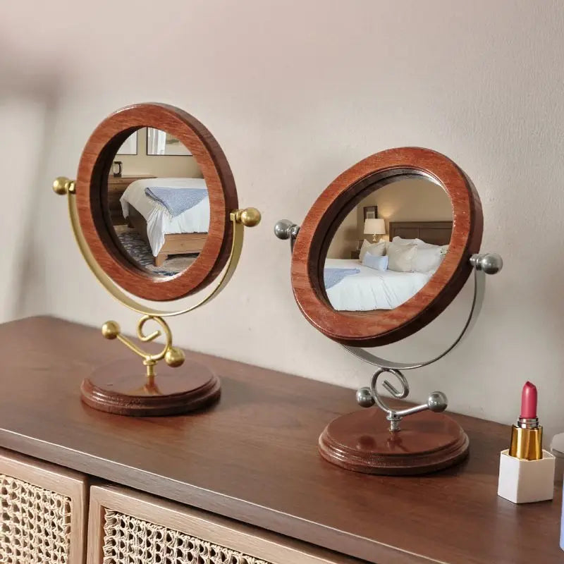 Two wooden and brass vanity mirrors on a dresser with a bedroom reflection.