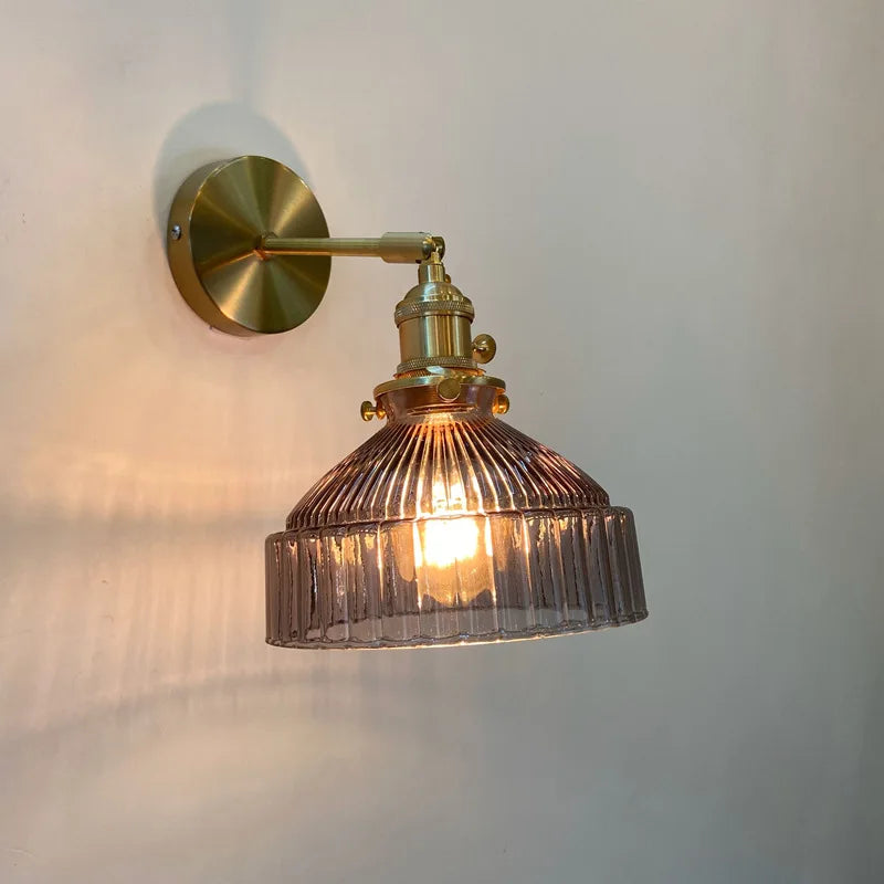 Wall-mounted lamp with brass fixture and ribbed glass shade on a white wall.