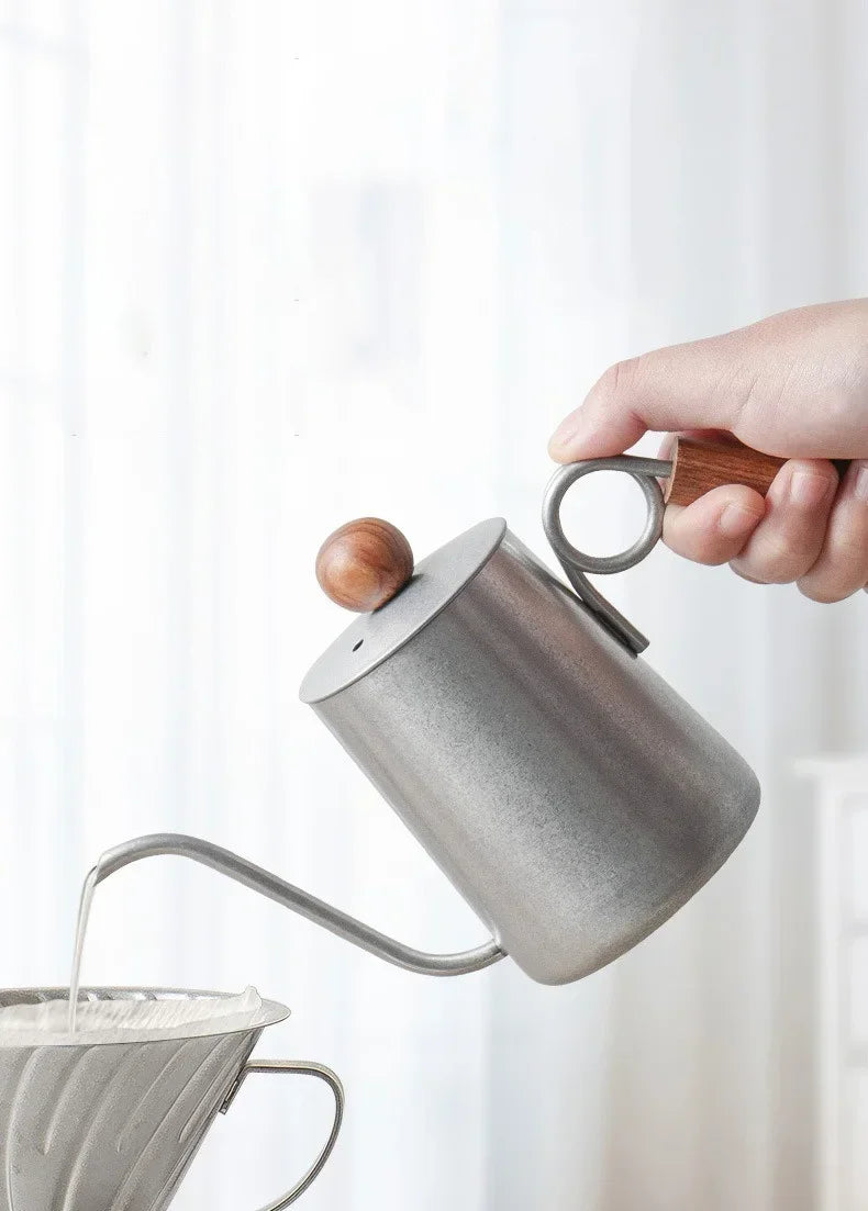 Person pouring coffee from a gray ceramic kettle with wooden handle on a white background