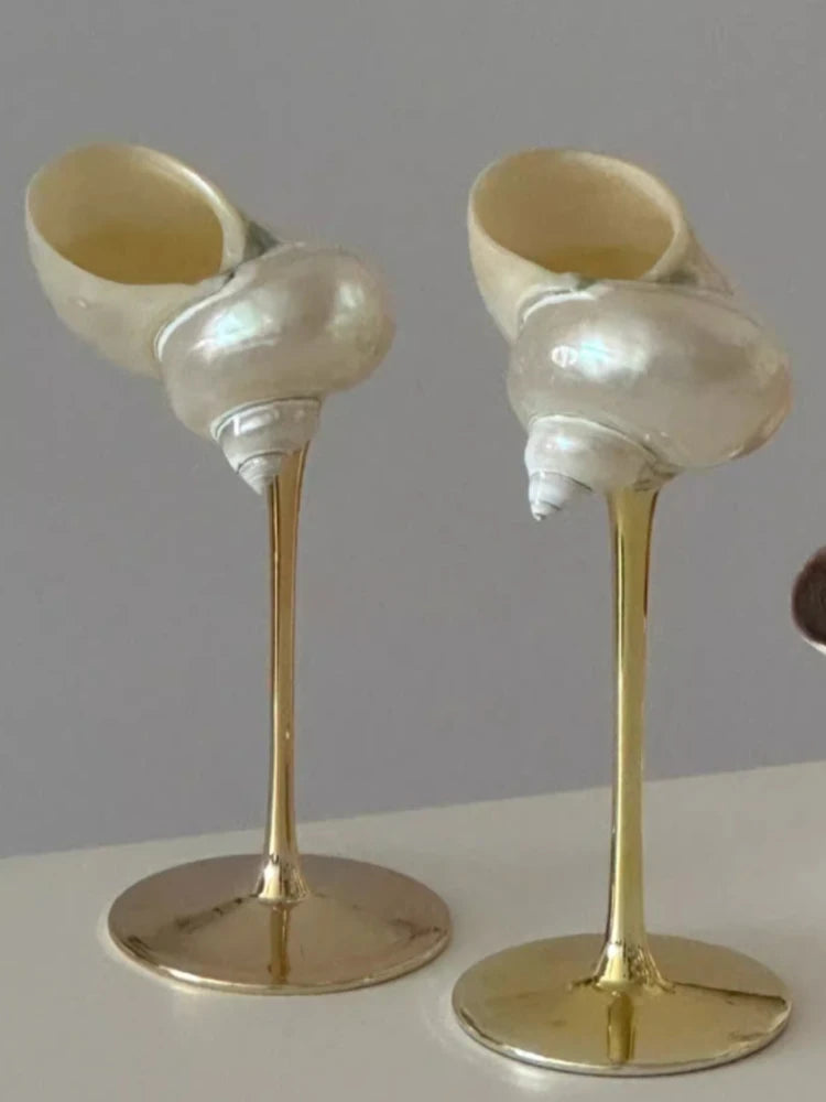Two decorative items resembling seashells on gold stands against a gray background