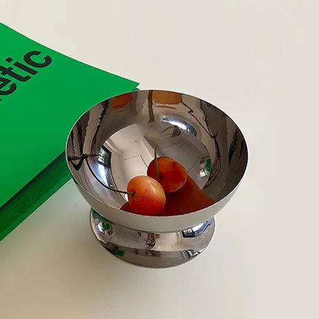 Silver bowl with fruits on a white surface next to a green book