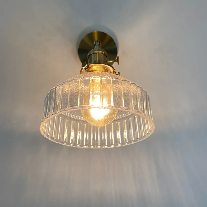 Ceiling light fixture with glass shade and gold fixture on a white wall