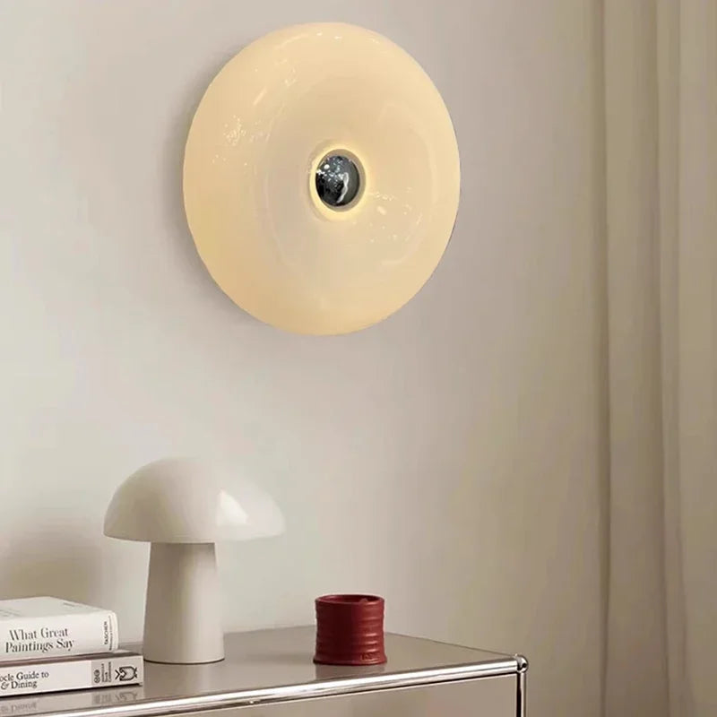 Round wall light fixture on a neutral wall with a table and books in the foreground.