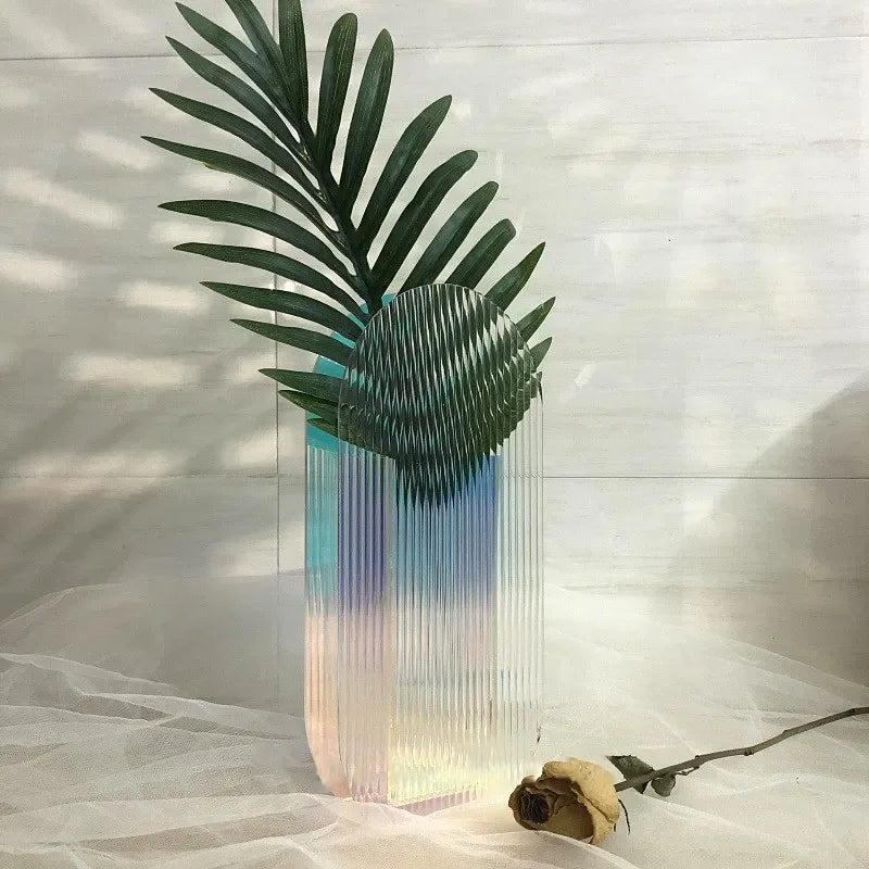 A cylindrical pink and blue ribbed vase on white backdrop with a yellow rose next to it