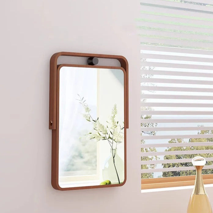 Rectangular mirror with wooden frame on a wall next to a window with blinds.