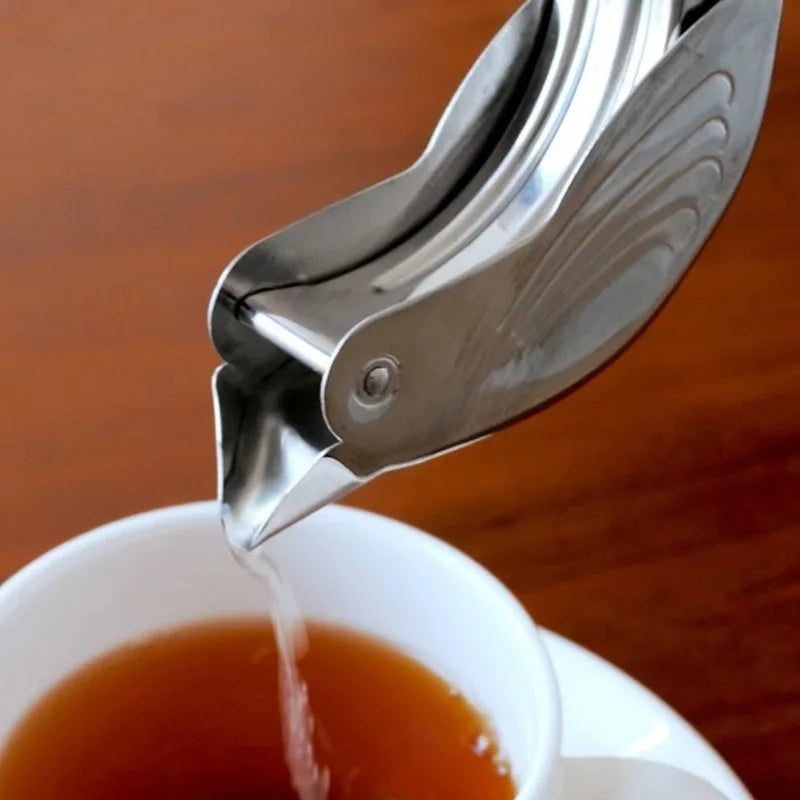 Metallic tea infuser being used to pour tea into a white cup on a wooden surface.