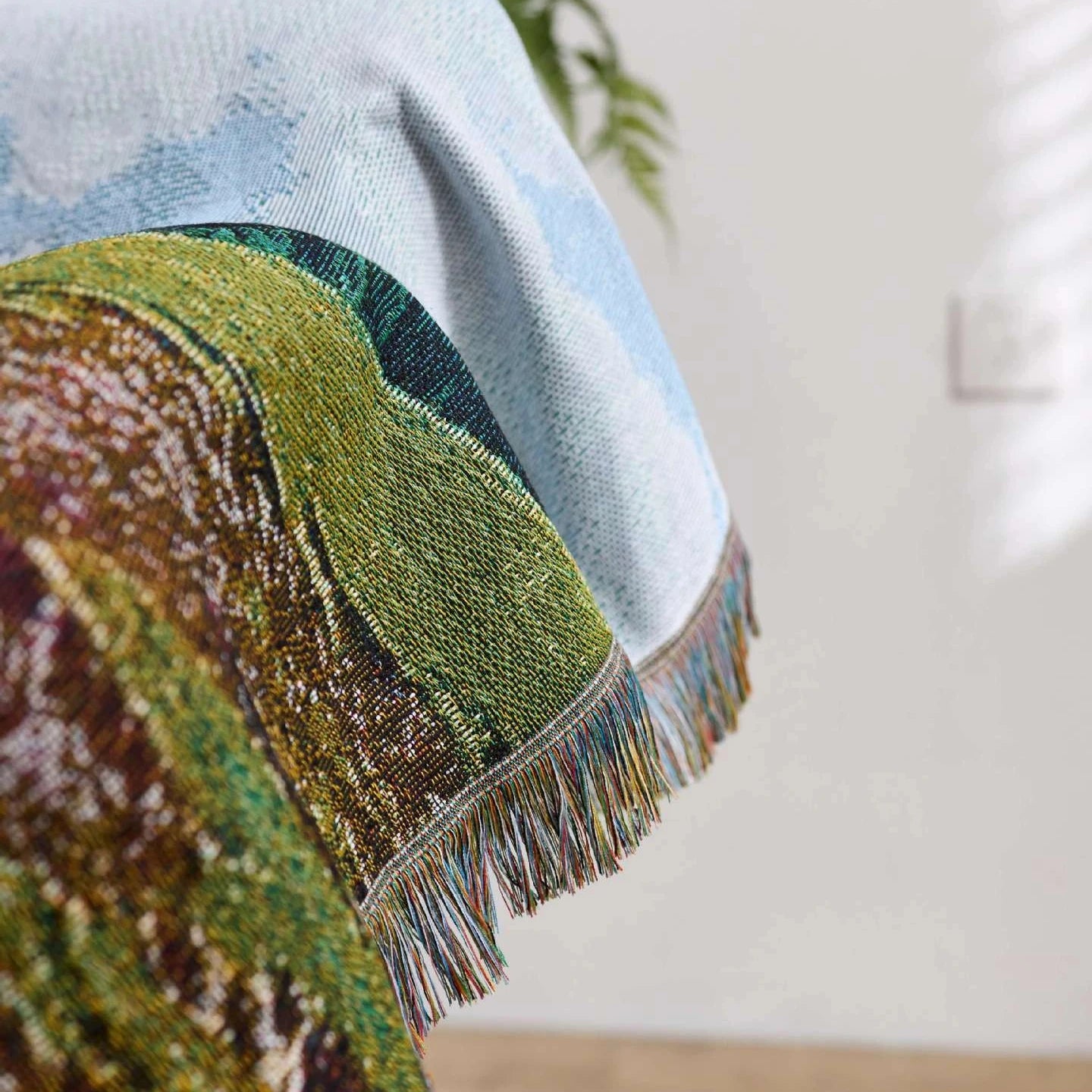 Close-up of a textured fabric with colorful patterns and fringes on a neutral background.