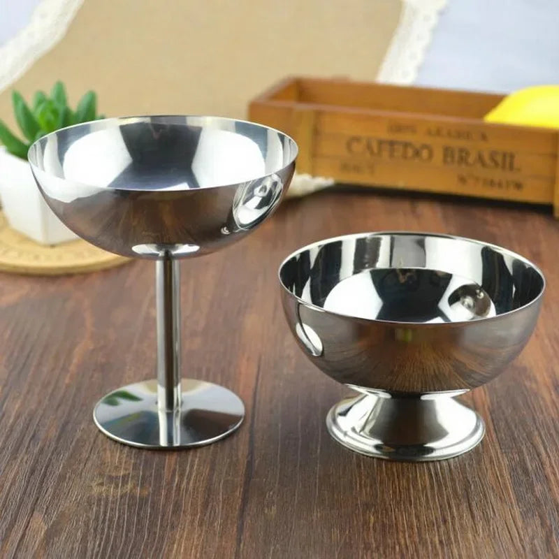 Two metallic pedestal bowls on a wooden surface with a blurred background.