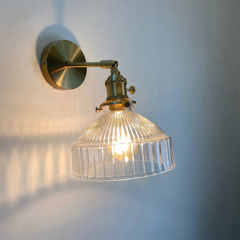 Wall-mounted light fixture with clear glass shade and brass finish on a white wall.