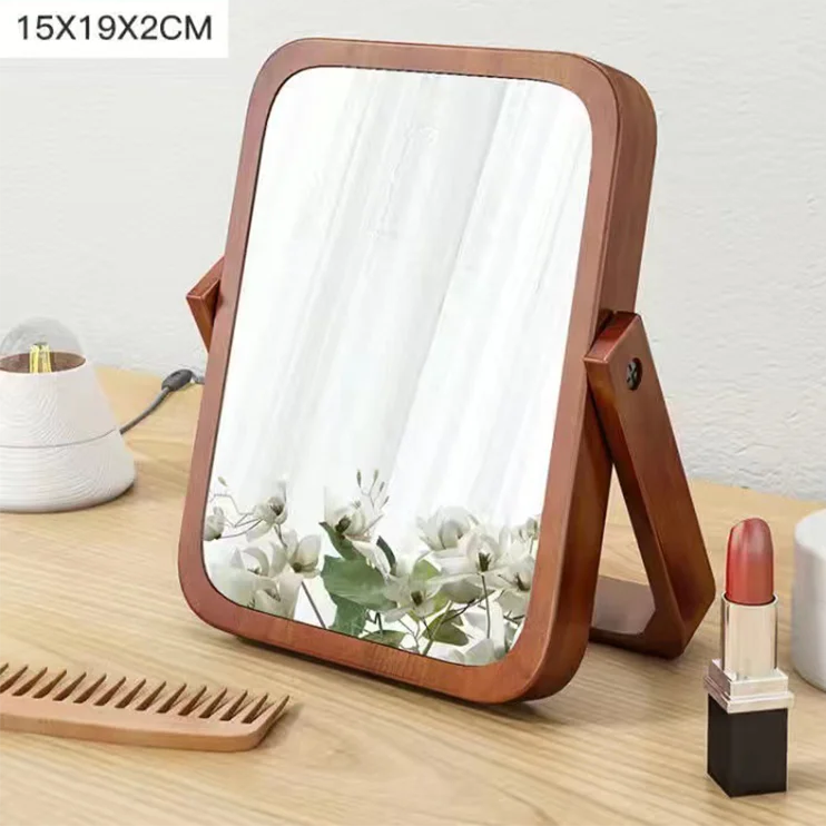 Wooden folding mirror on a wooden surface with a lipstick and other items.
