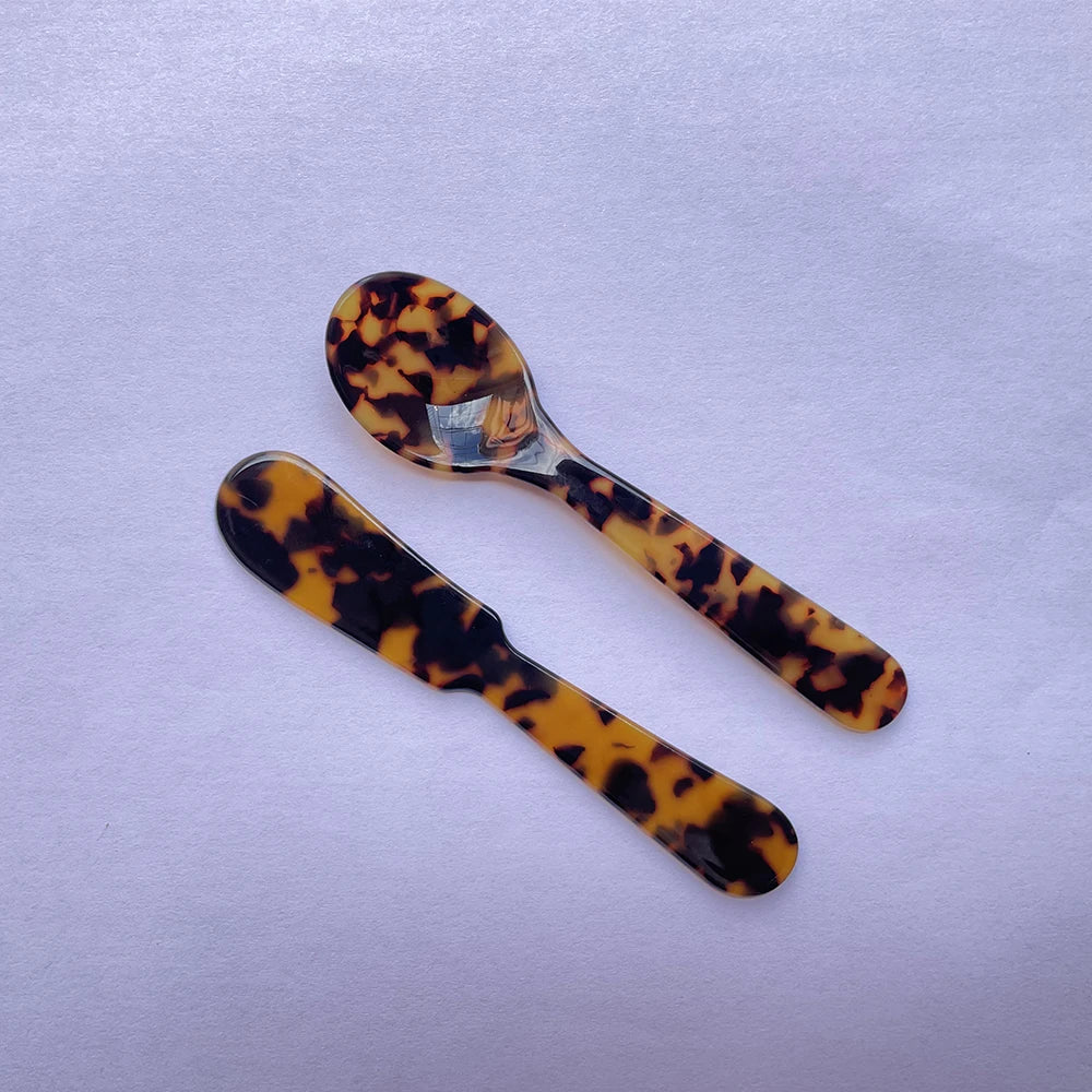 Two tortoiseshell patterned spoons on a light purple background