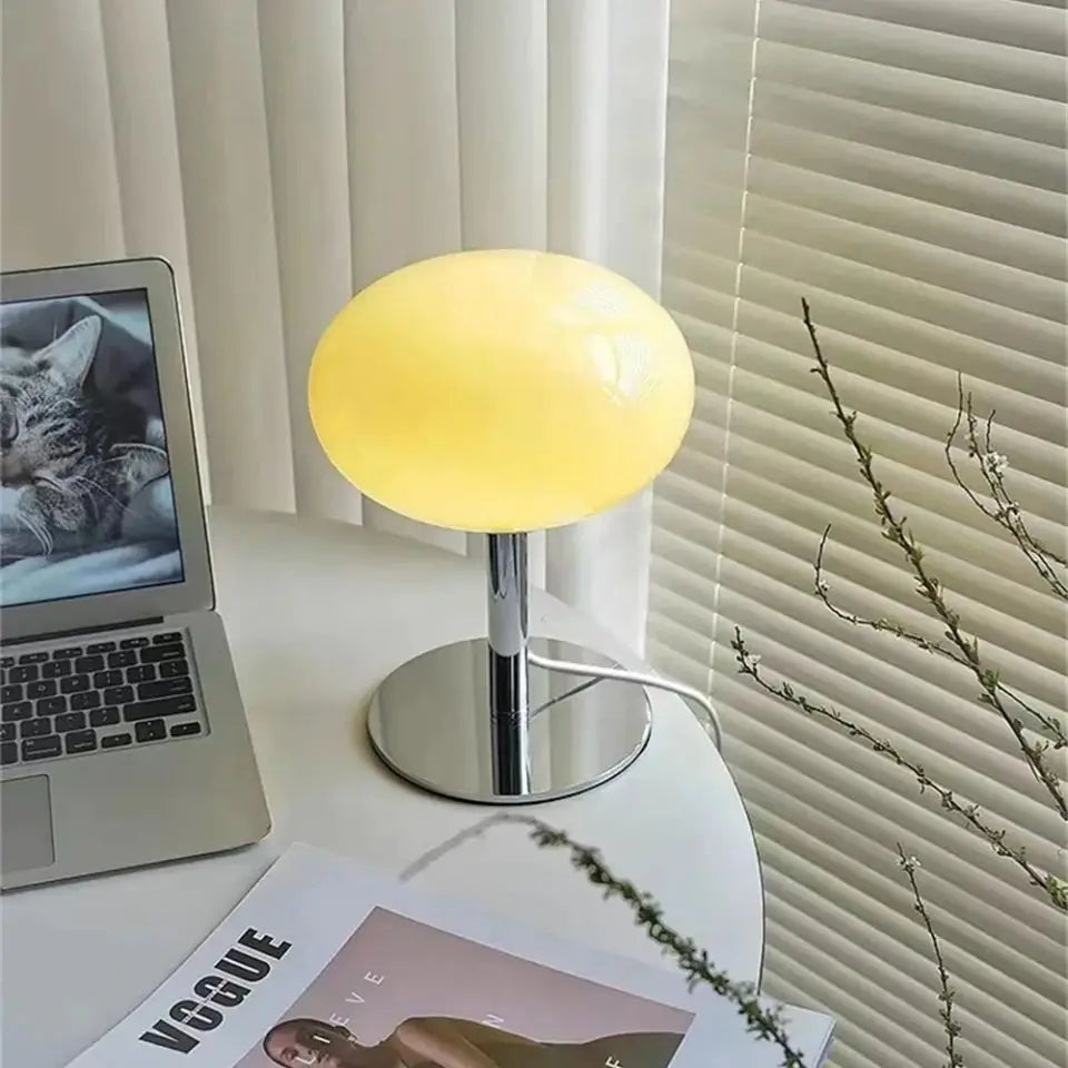 Yellow table lamp on a desk with a laptop and magazine in the background