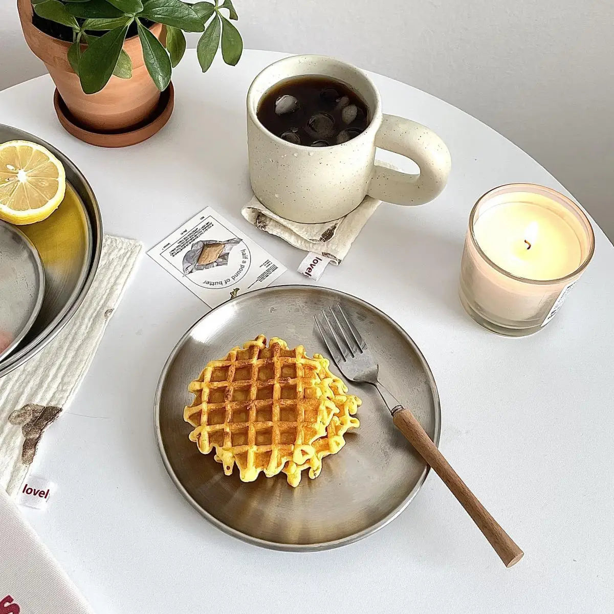 Waffle on a plate with a fork, cup of coffee, and candle on a table.