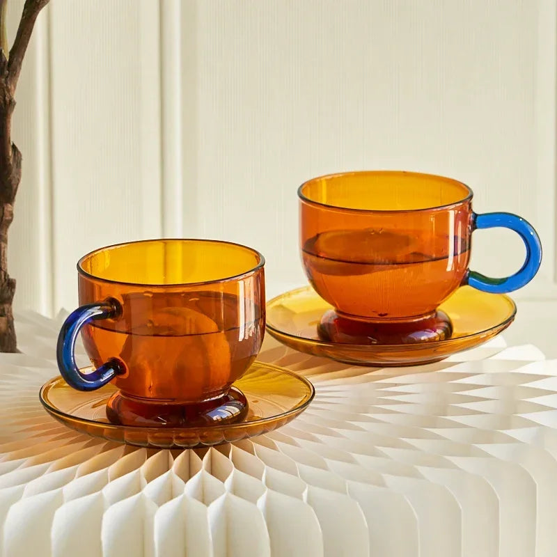 Two amber glass cups with blue handles on matching saucers against a neutral background