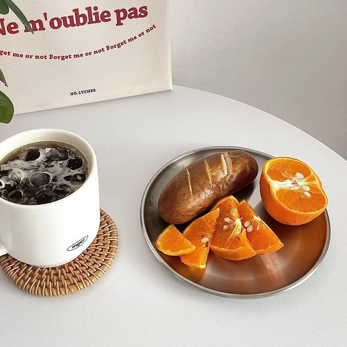 White mug with dark liquid, sliced orange, and bread on a metal tray on a white surface.