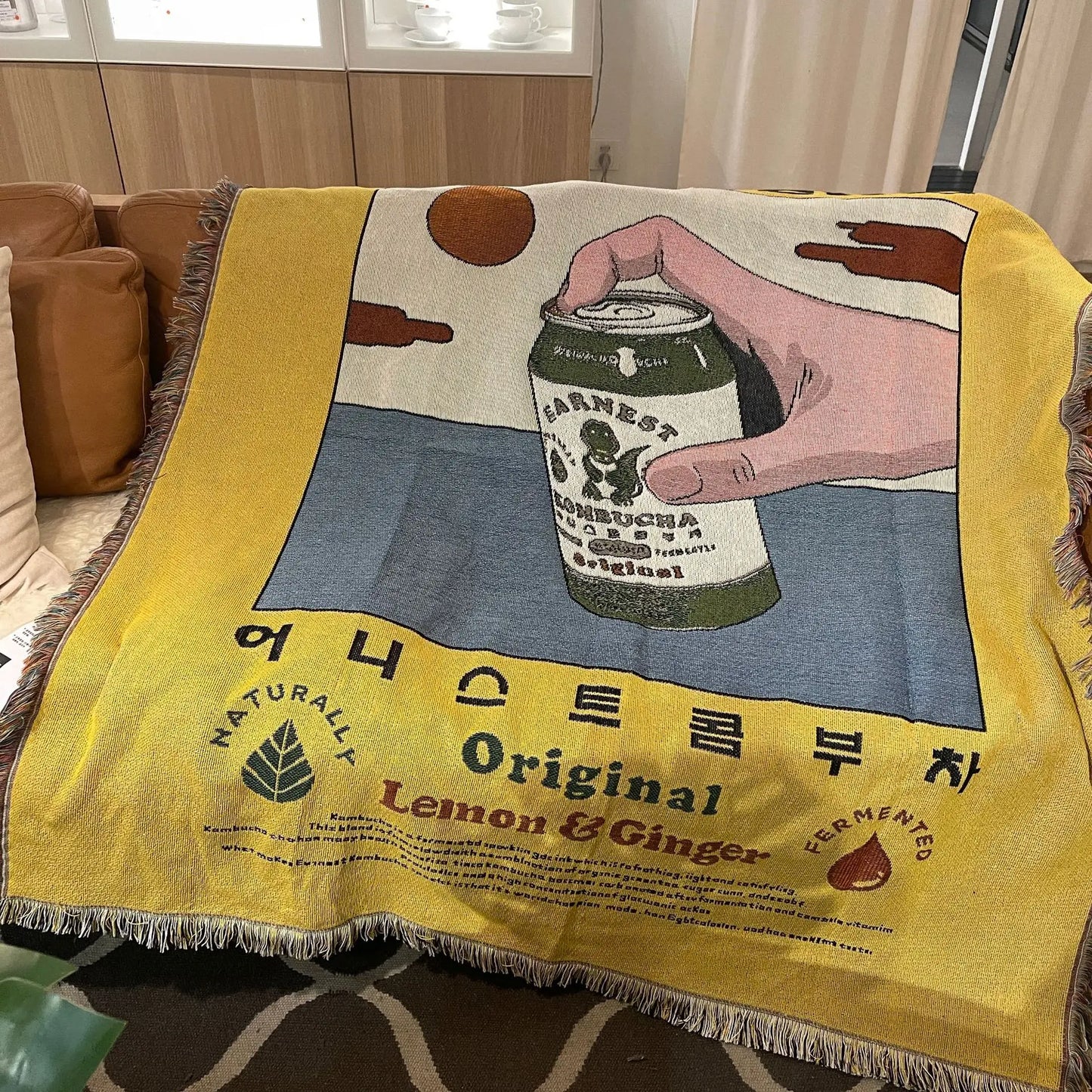 Blanket with a design of a hand holding a can labeled 'Earnest' on a yellow background.
