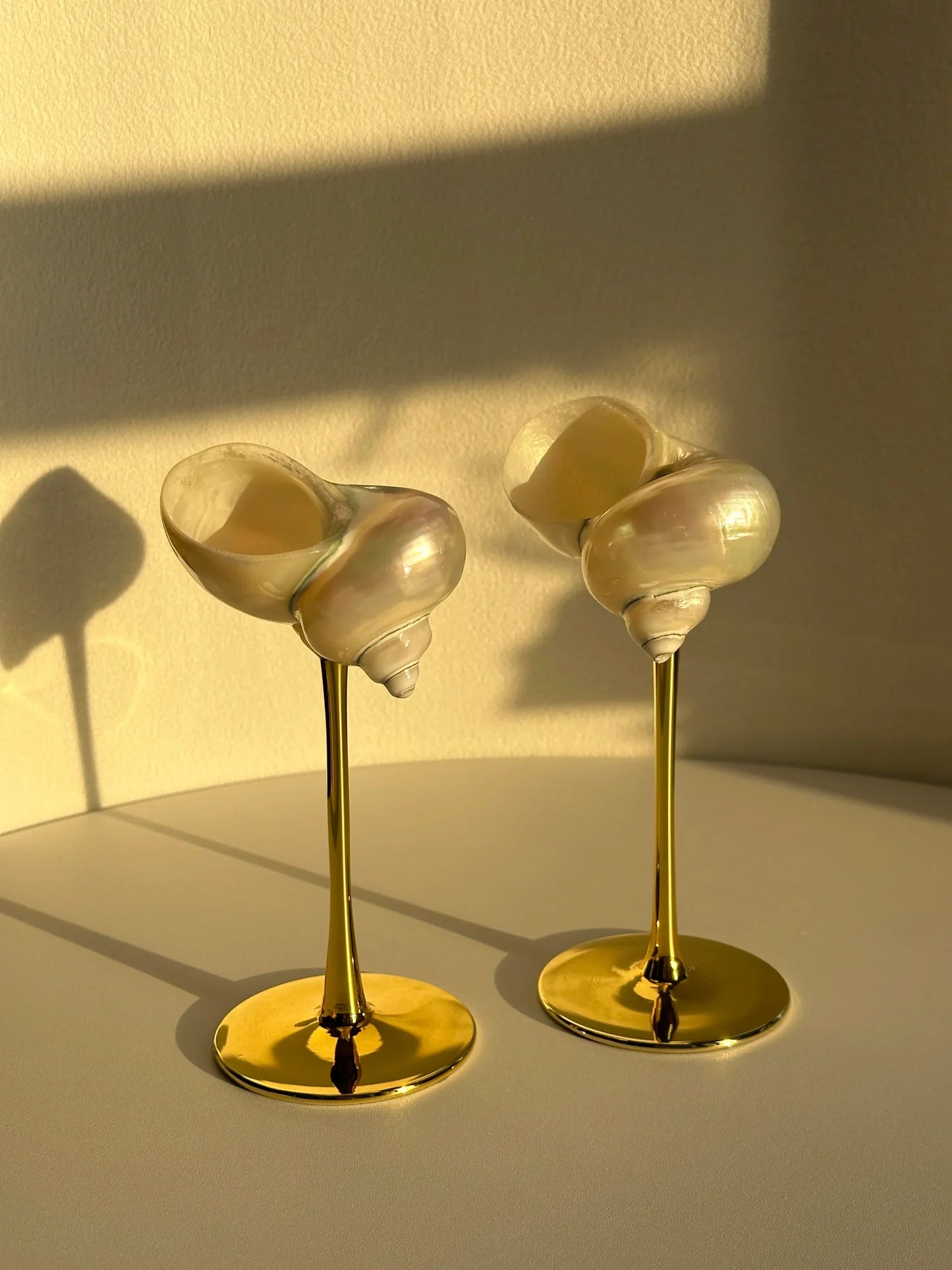 Two shell-shaped objects on gold stands against a beige background