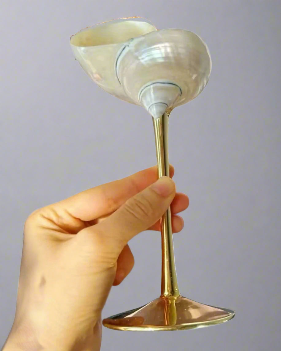 Hand holding a shell with a gold stem against a plain background