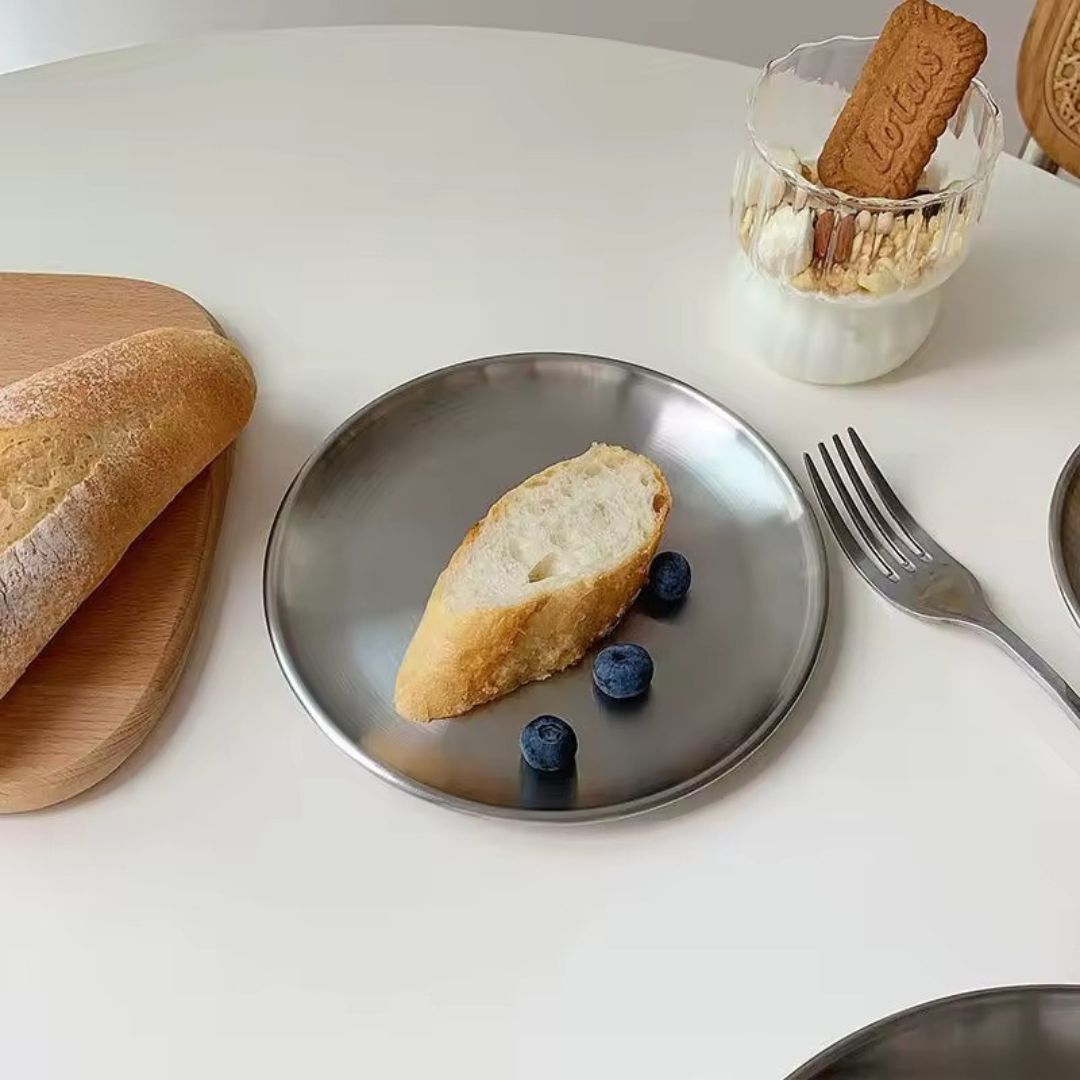 Bread slice with blueberries on a metal plate, with a glass of milk and cookies in the background.