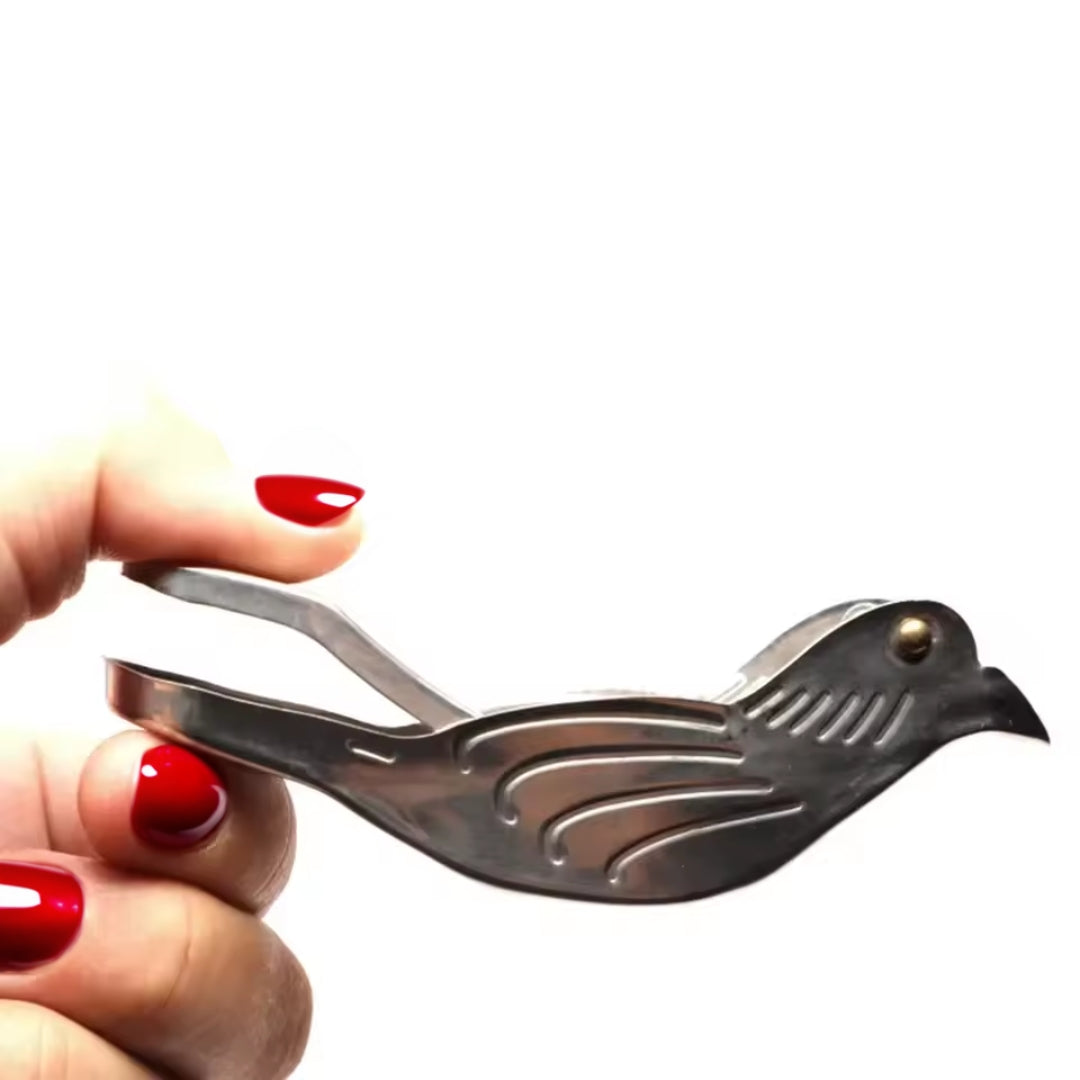 Metallic bird-shaped tool held by a hand with red nail polish on a white background