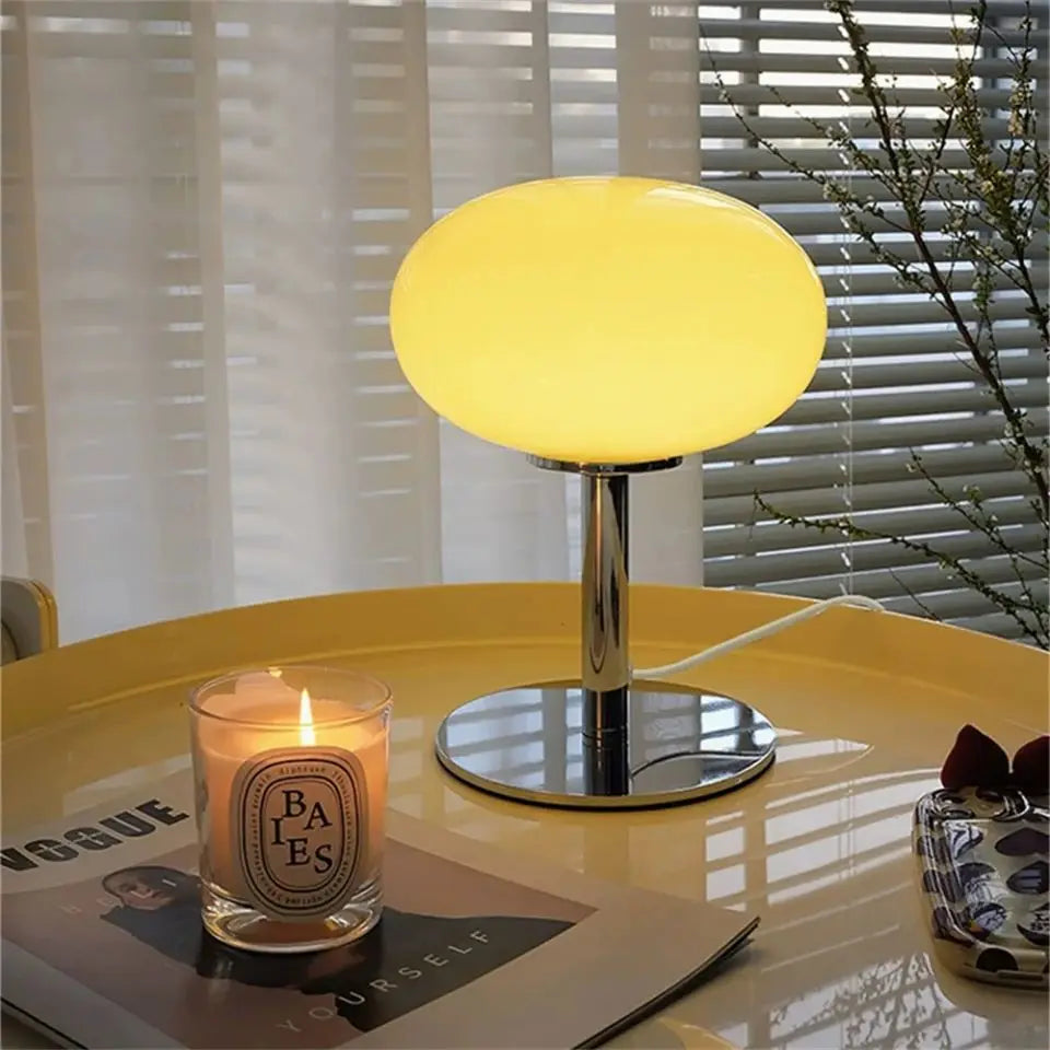 Yellow table lamp on a round table with a lit candle and magazine in the background.
