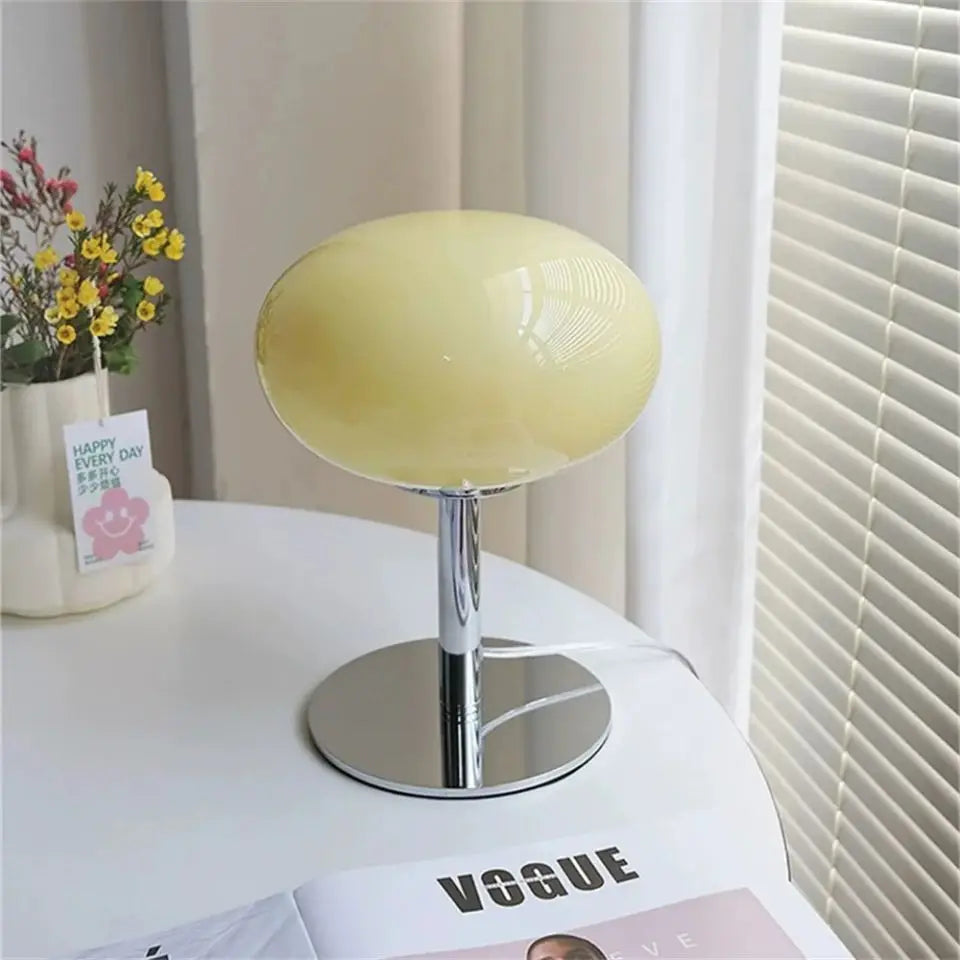 Yellow spherical lamp on a white surface with a magazine and small plant in the background.