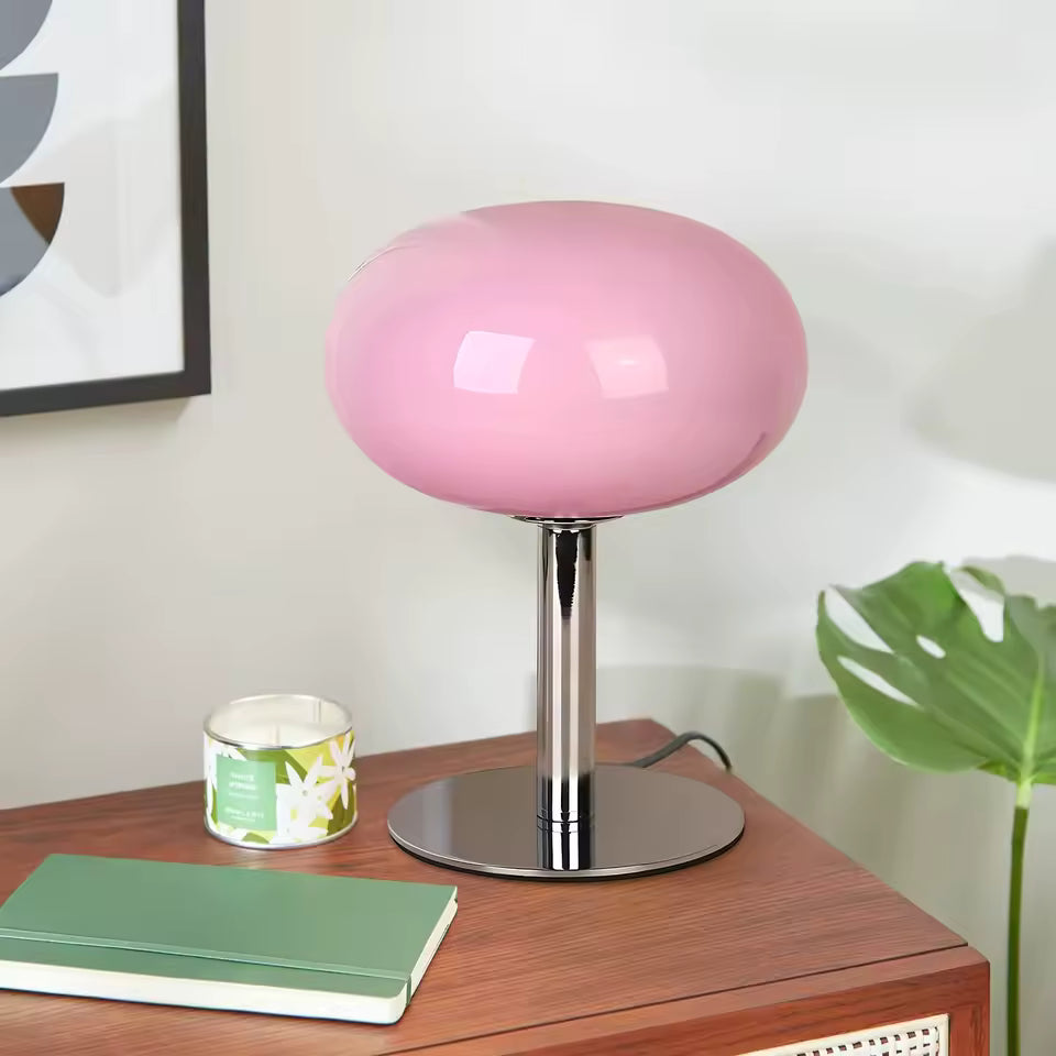 Pink table lamp on a wooden surface with a notebook and candle
