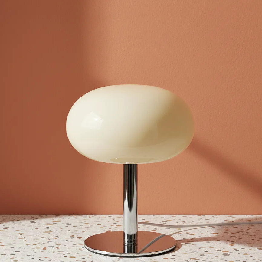 Table lamp with a white shade and chrome base on a terrazzo countertop against a peach wall.