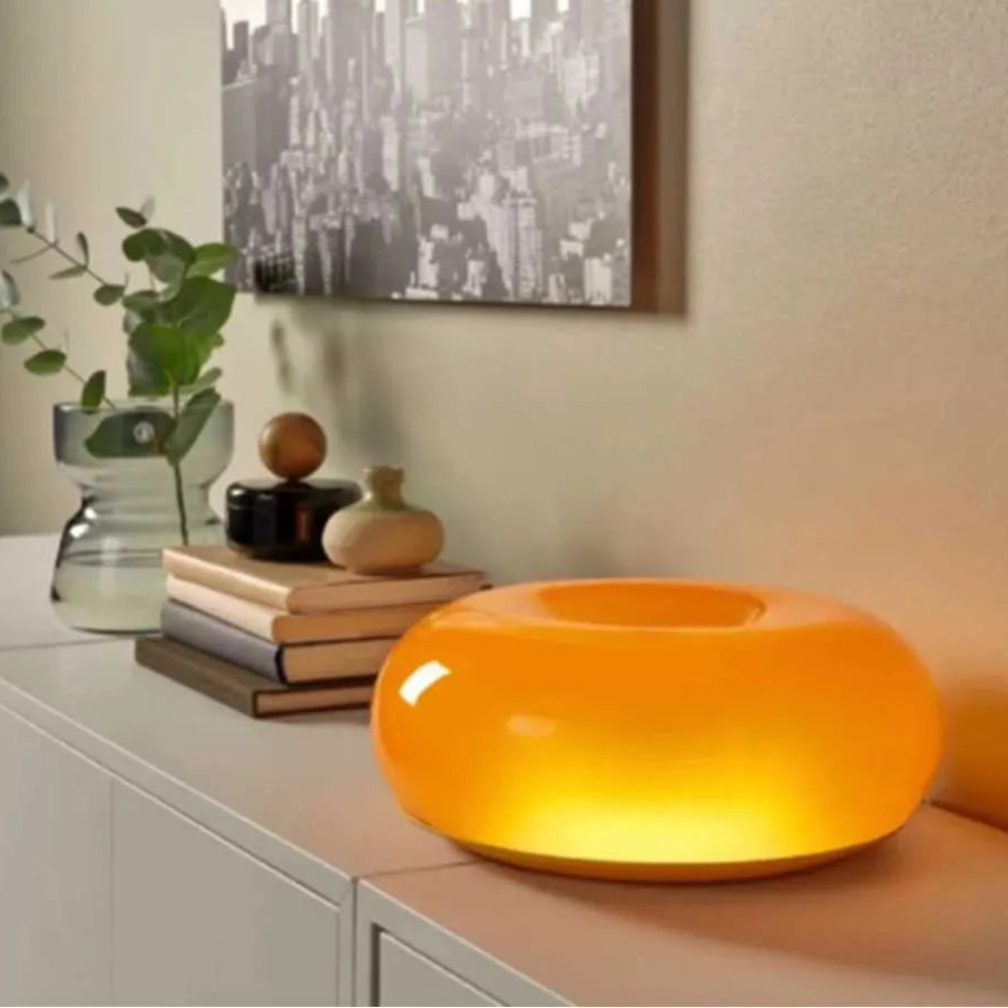 Orange table lamp on a surface with decorative items and a cityscape painting in the background.