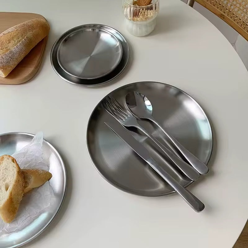 Stainless steel plates with cutlery on a white table with bread slices.