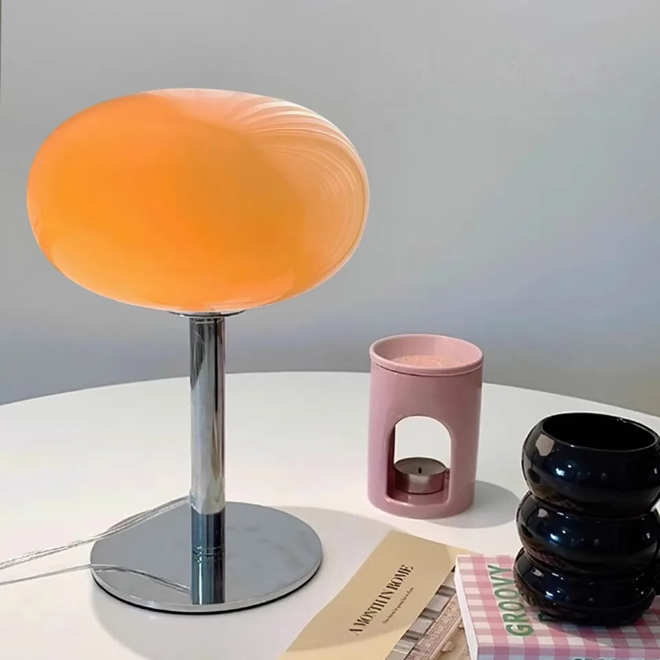 Orange table lamp on a white surface with a pink container and black vase.