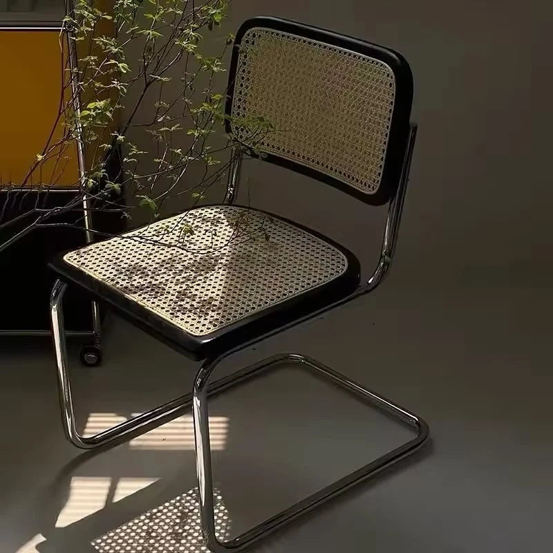 A rattan chair with metal legs and a plant nearby.