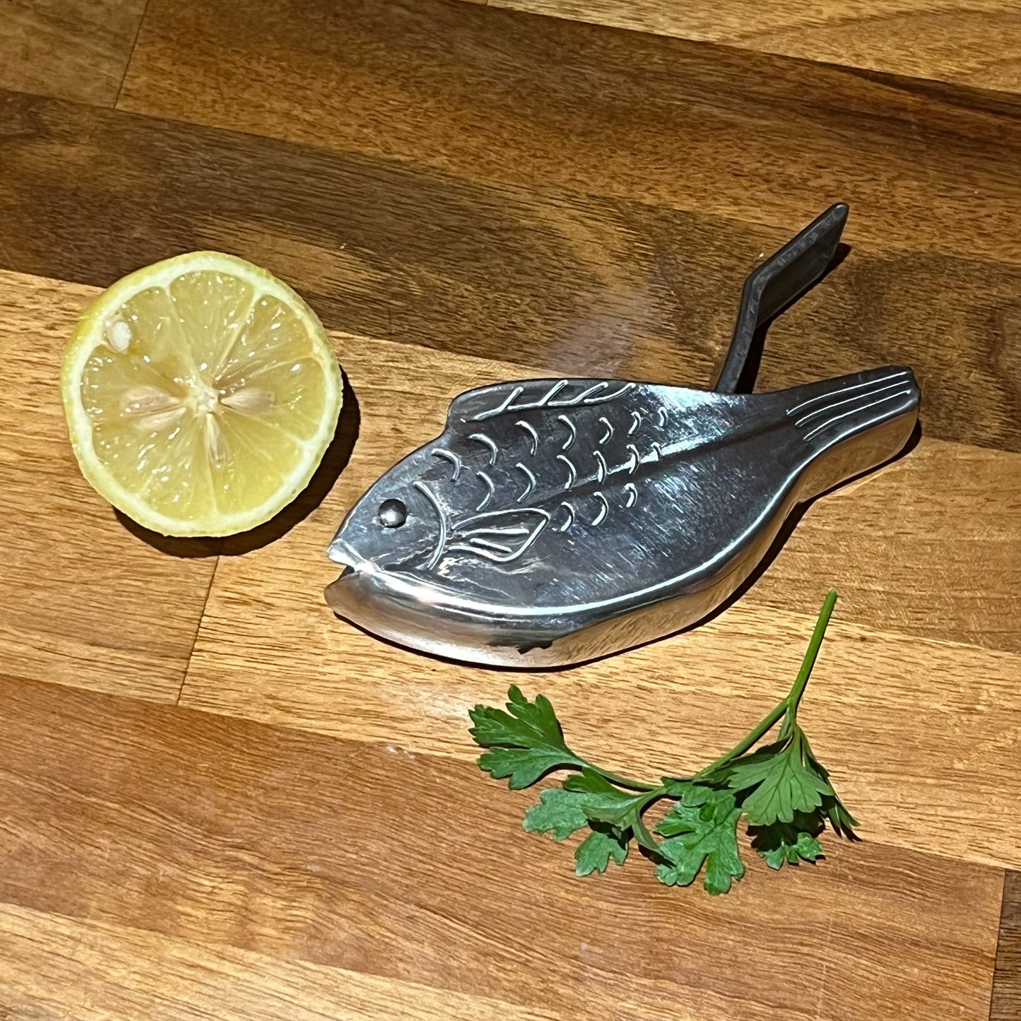 Metal lemon squeezer on a wooden surface with a half-sliced lemon and fresh parsley.