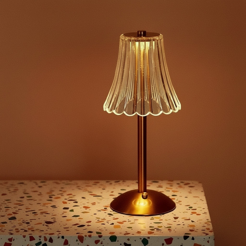 A glass table lamp on a terazzo surface ommiting a warm light.