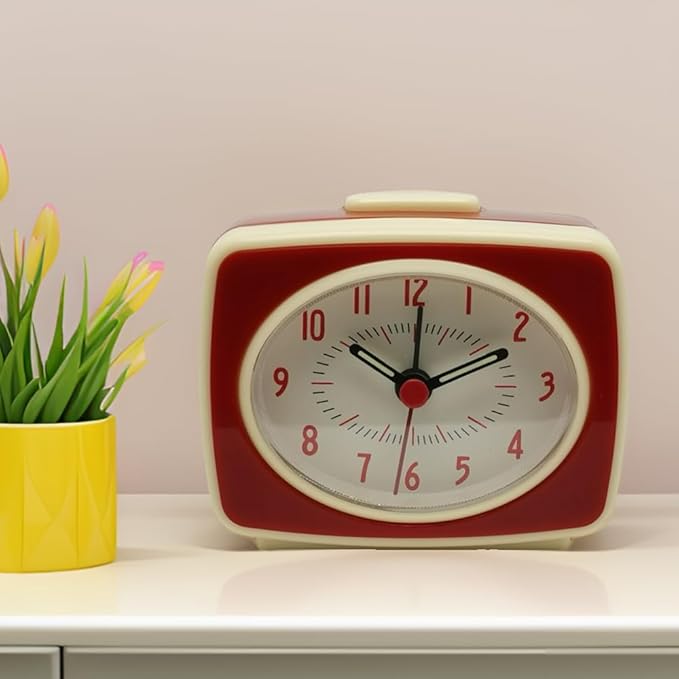 Vintage-style red and white clock on a shelf with a yellow vase containing green plants.